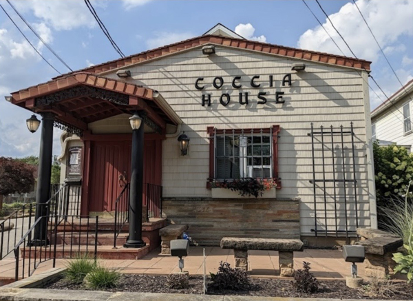 coccia-house - St. Paul Hotel | Boutique Hotel Wooster Ohio Front view of a small beige building labeled 'COCHIA HOUSE' with a red door, covered porch, and potted plants outside.
