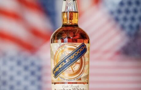 - St. Paul Hotel | Boutique Hotel Wooster Ohio Bottle of Minglewood Bourbon Whiskey on a metal surface with a blurred American flag background, showcasing the label and 115 proof.