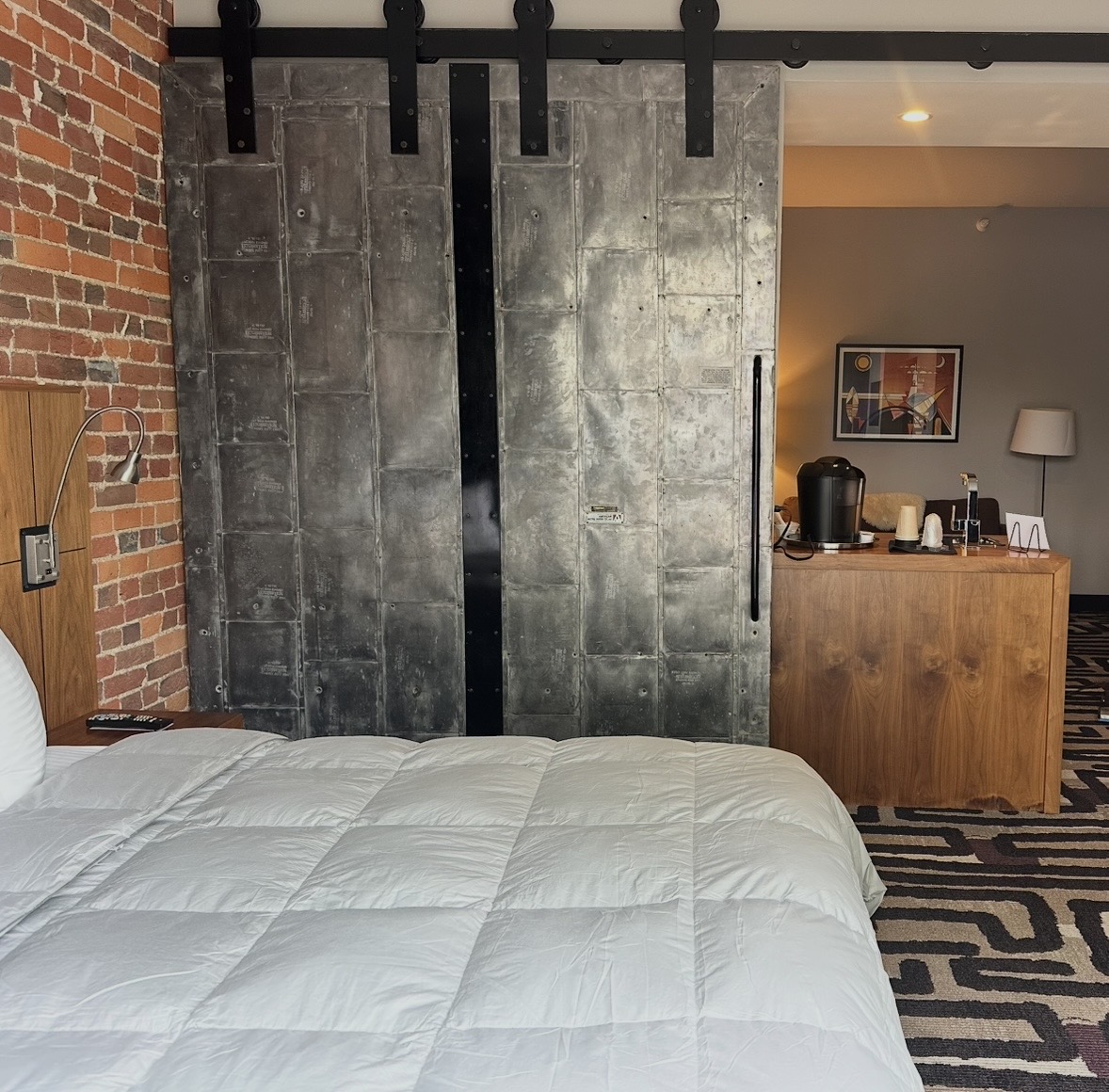 grand-suite - St. Paul Hotel | Boutique Hotel Wooster Ohio Hotel room with a metal sliding barn door, brick accent wall, and a white comforter in the foreground.